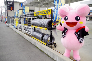 ドライバーに手を振るラブちゃん。交通量は多く、周りにはガソリンスタンドや車屋さんがたくさんあります。「24時間営業だよ！いつでも来てね♪」